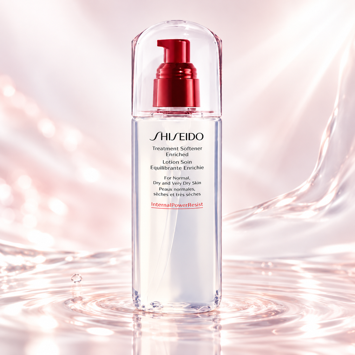Shiseido Treatment Softener Enriched in an elegant transparent bottle with a red pump and clear cap, displayed on a luminous blush-pink water surface with delicate ripples, flowing silky textures and soft reflections. Premium Japanese hydrating skincare for normal to very dry skin.