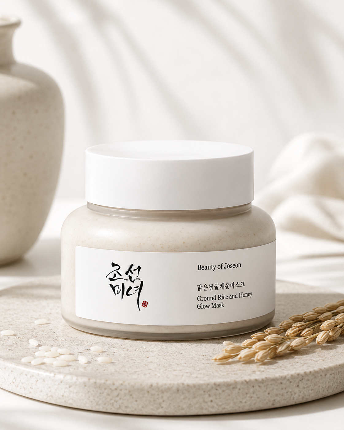Beauty of Joseon Ground Rice and Honey Glow Mask 150ml elegantly displayed on a natural stone tray in a warm spa-inspired setting with soft daylight, ceramic décor, rice grains and botanical elements, highlighting its nourishing, gently exfoliating and brightening formula that helps refine skin texture, deeply hydrate and reveal a healthy, radiant glow.